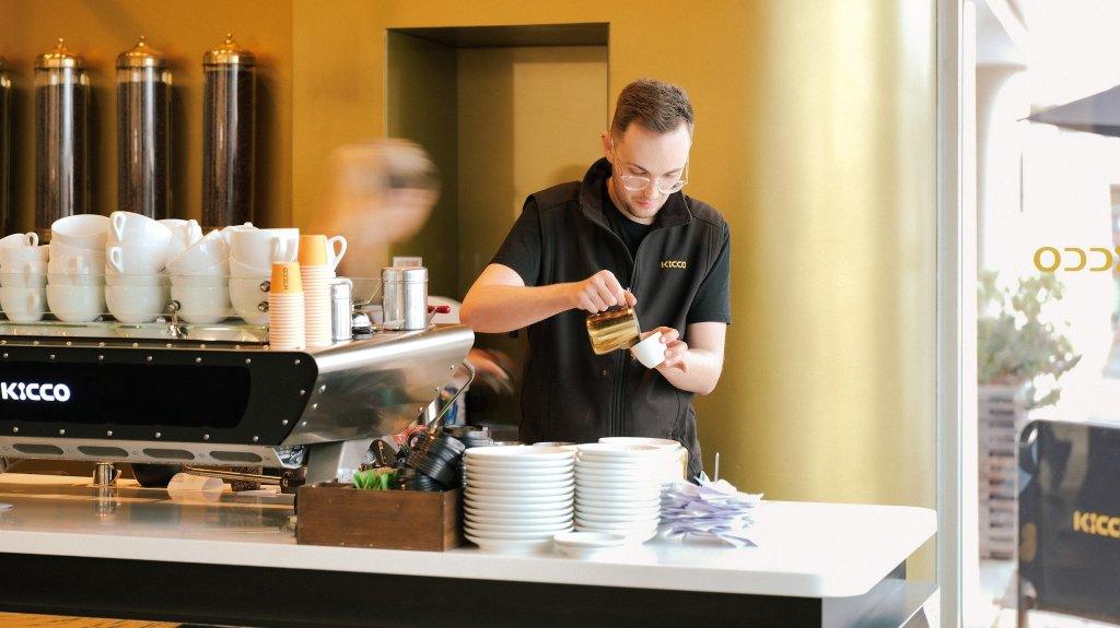 Kicco Coffee McLaren Vale Barrista making an espresso with cups stacked on top of the coffee machine and the orders dockets and plates in for foreground