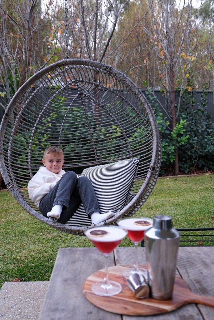 Vale 194 McLaren Vale Family accommodation boy relaxing in backyard in hanging chair cocktails on table for adults